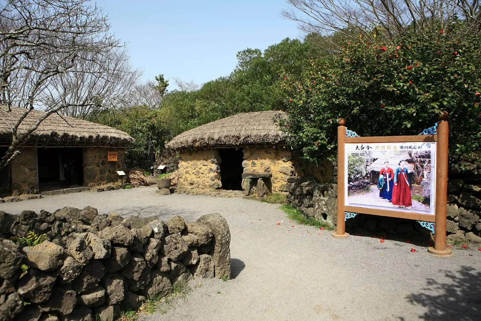 Traditional houses and a Dae Jang Geum scene panel at Jeju Folk Village.